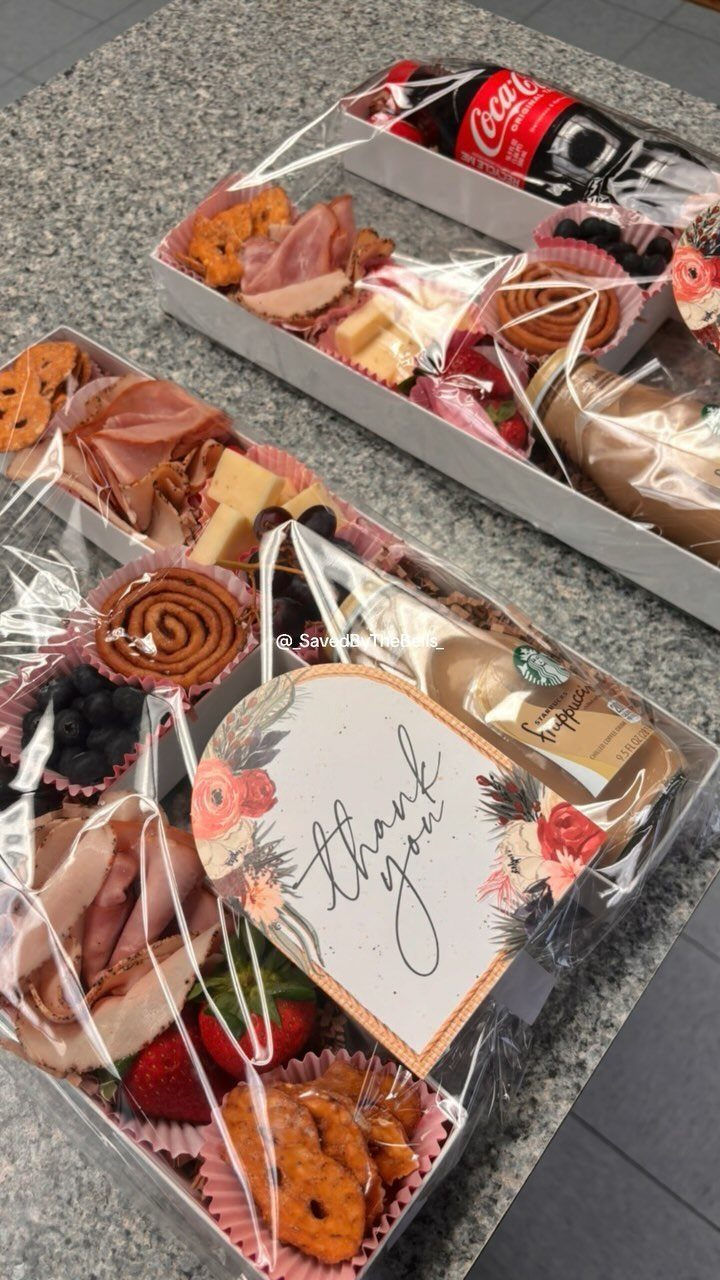Two snack gift boxes with meats, cheeses, and fruit wrapped in clear cellophane.