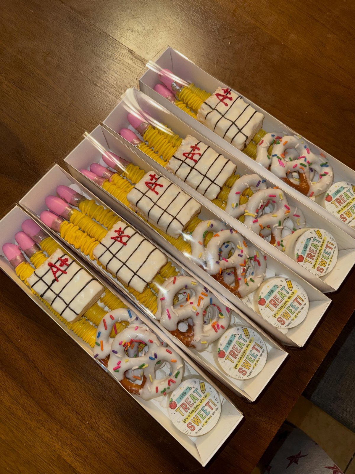 Four gift boxes containing A+ notebook treats and sprinkle-covered pretzels on wood.