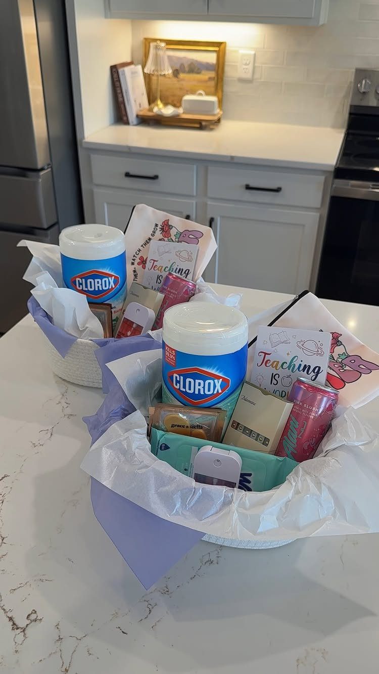Two white gift baskets filled with cleaning wipes, snacks, and teacher-themed cards.
