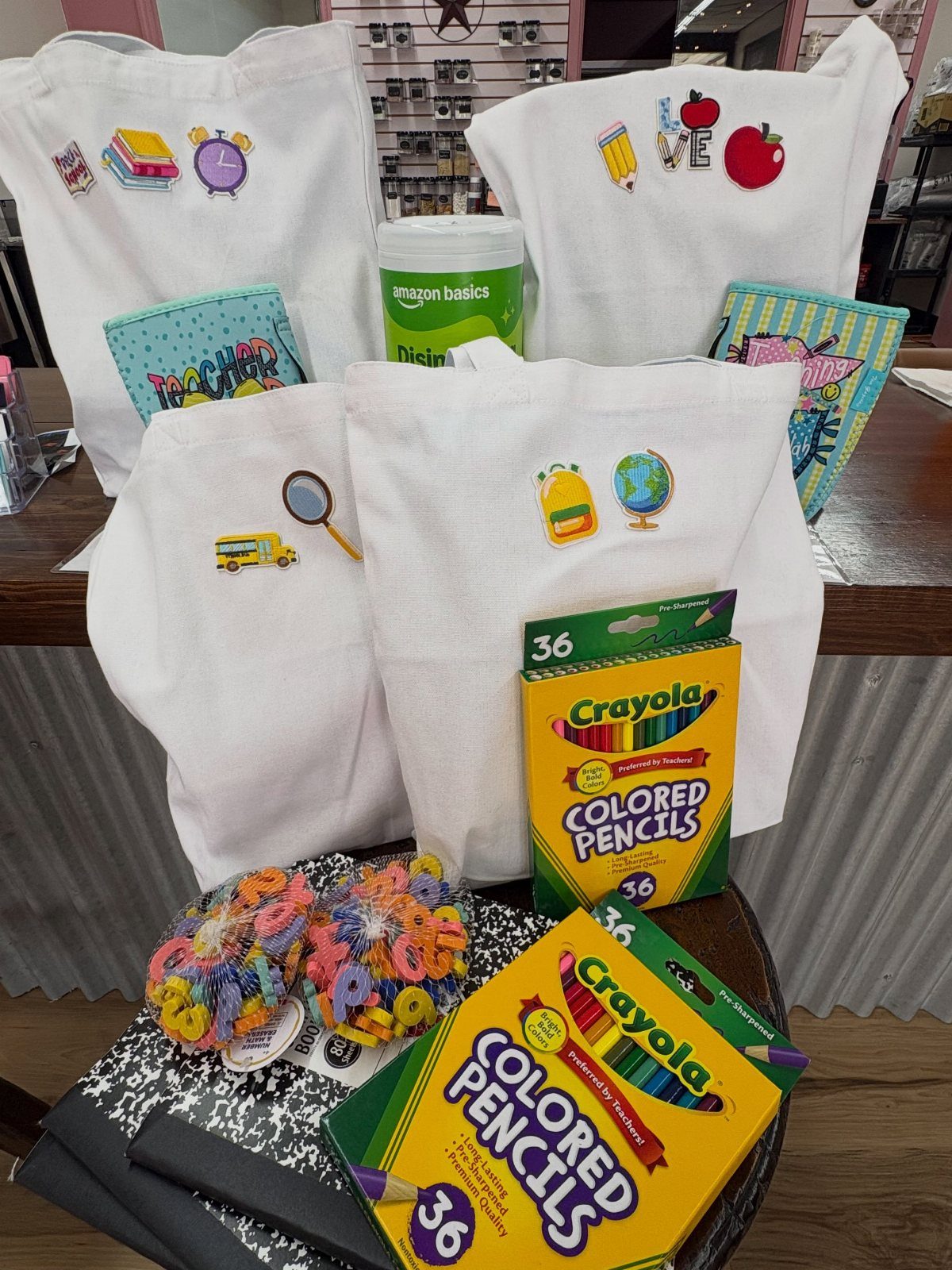 White fabric gift bags with school stickers and Crayola colored pencils on a table.