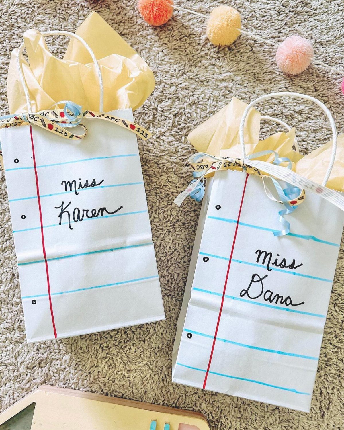 Two notebook paper themed gift bags labeled Miss Karen and Miss Dana with ribbons.