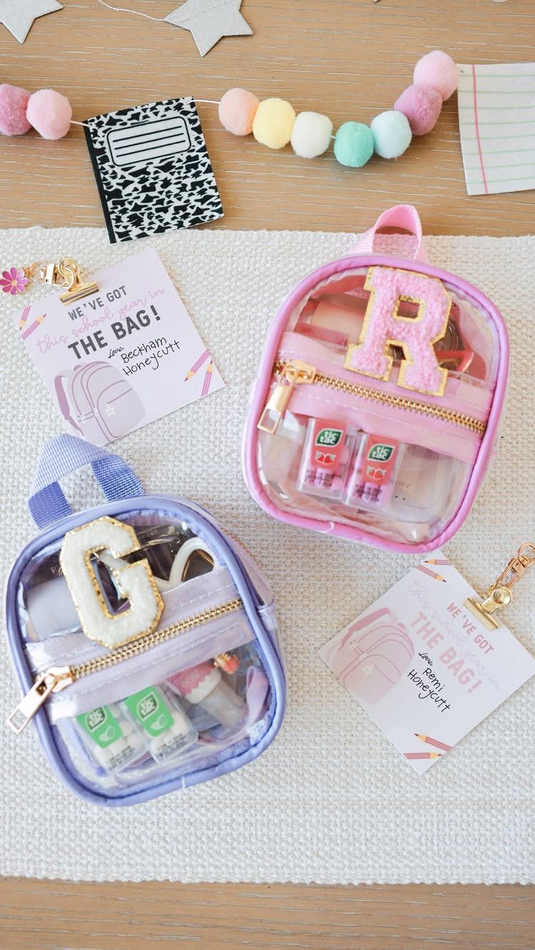 Two clear zippered pouches with glittery letters and gift tags on a white mat.