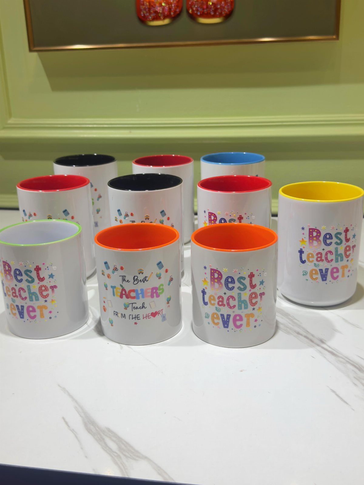 White ceramic mugs with colorful interiors and Best teacher ever text on marble surface