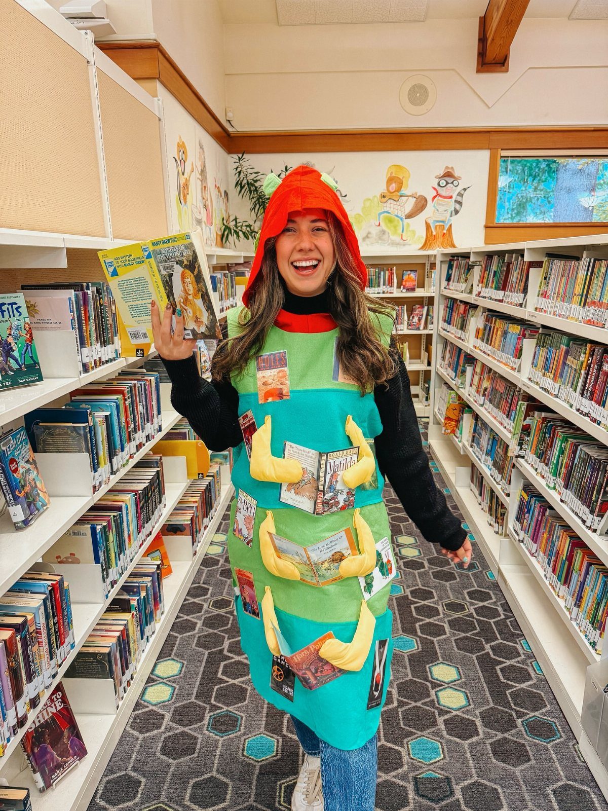 Woman in a bookworm costume holding a book in a school library