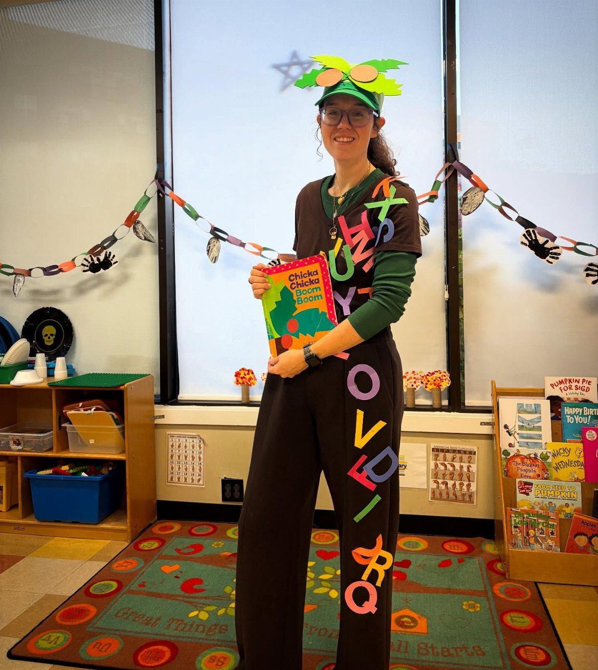 Woman wearing a coconut tree costume with colorful letters holding a children's book.