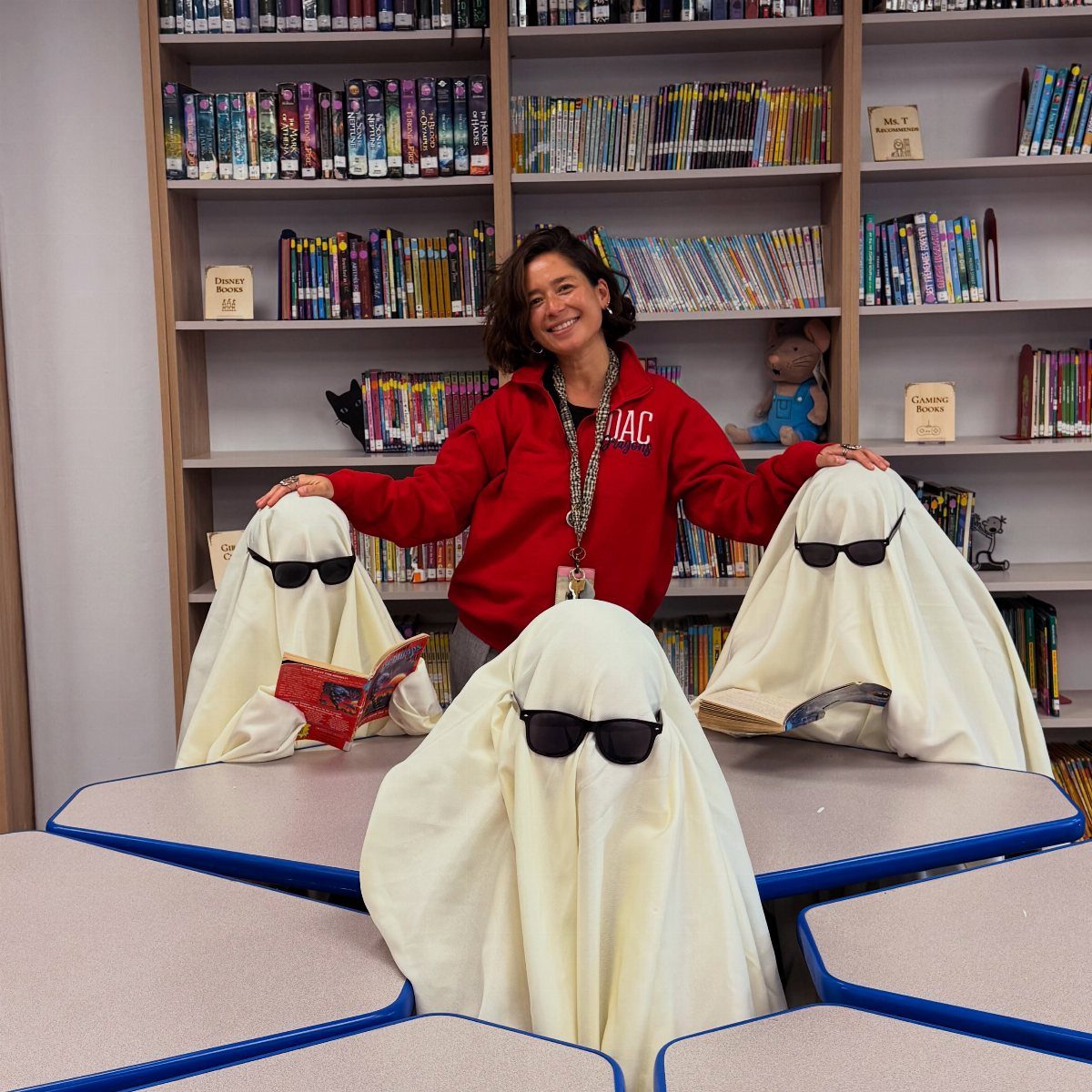 Woman in red hoodie with three ghosts wearing sunglasses in a school library.
