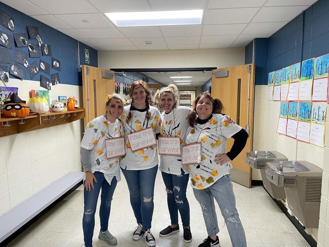 Four women in a school hallway wearing Field Trip Survivor t-shirts and jeans.