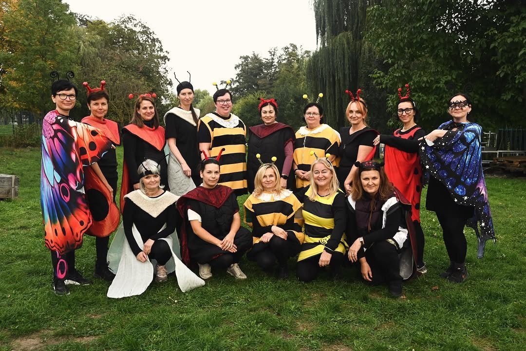 Group of women wearing bee, butterfly, and ladybug costumes posing on green grass.