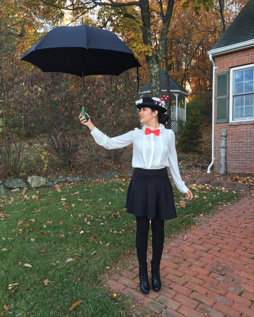 Woman in Mary Poppins costume holding a black umbrella on a brick path