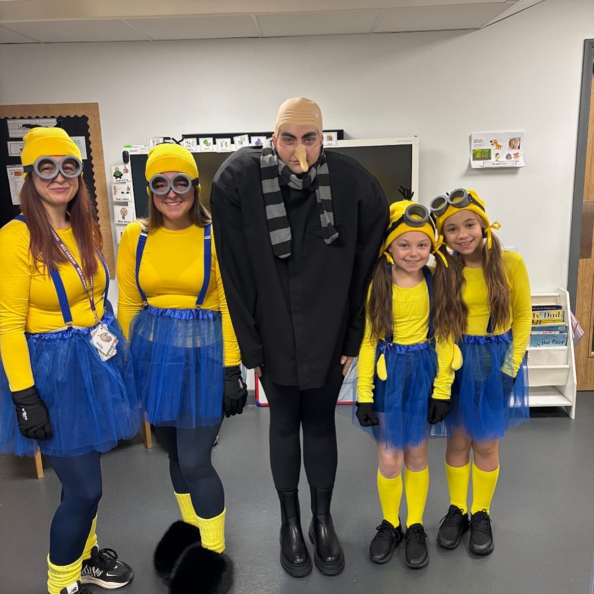 Group of people dressed as Minions and Gru posing in a classroom.