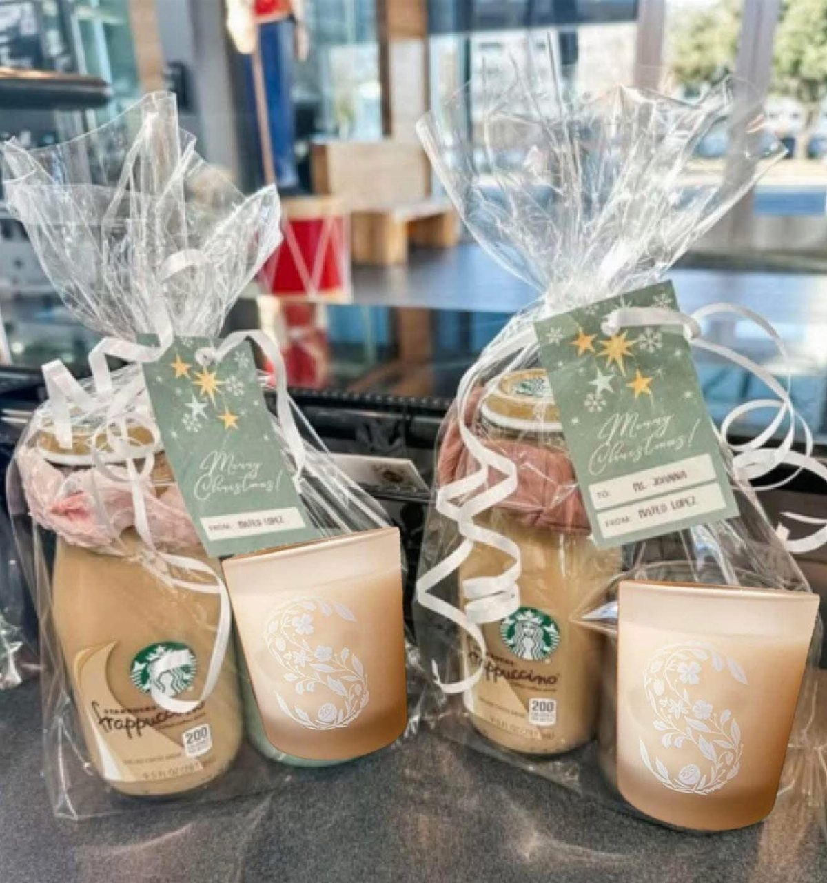 Two gift bags containing Starbucks bottled coffee and gold candles with Christmas tags.