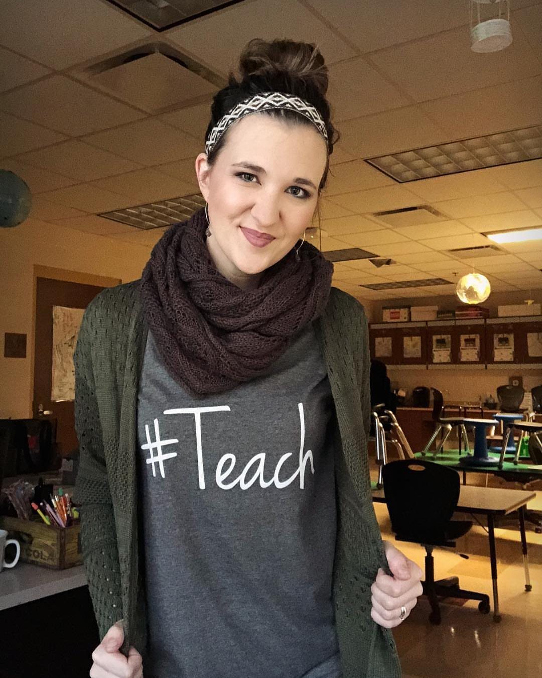 Woman wearing a brown knit infinity scarf and a grey teacher t-shirt.