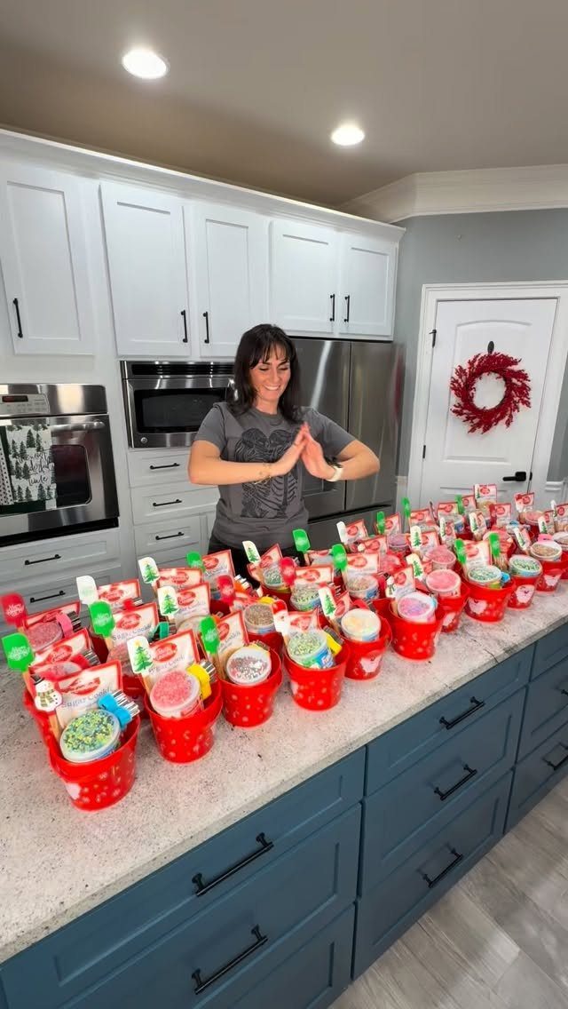 Woman standing behind a kitchen counter filled with many red holiday gift buckets.