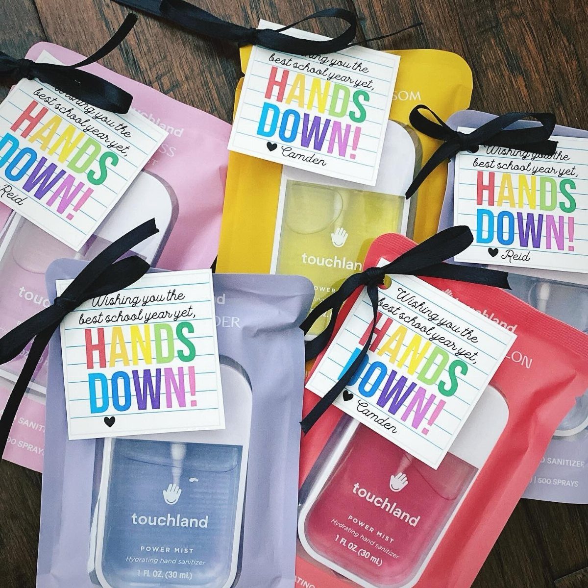 Colorful hand sanitizer sprays in fabric pouches with personalized gift tags on wood.