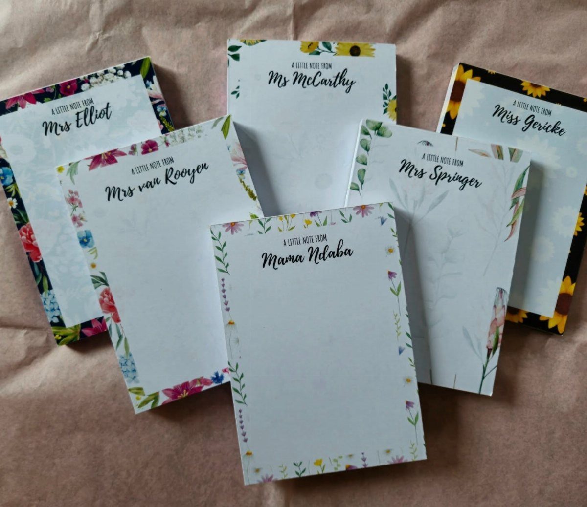 Personalized floral note cards with teacher names scattered on a brown background.