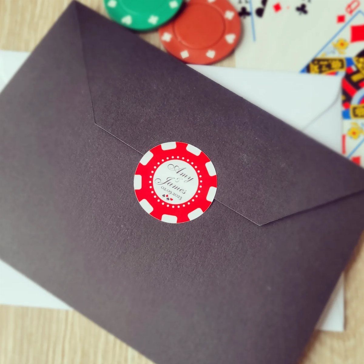 Dark purple envelope with a poker chip seal and gambling accessories in background