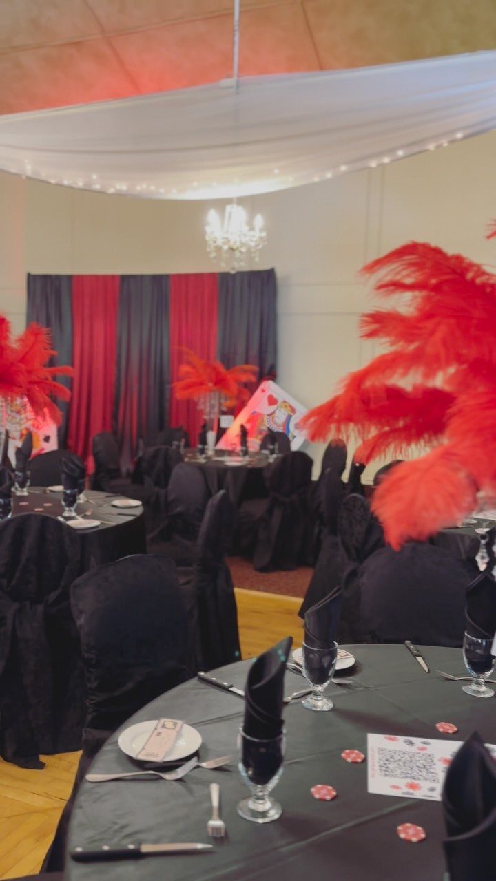 Banquet room with black tables, red feather centerpieces, and red and black curtains.