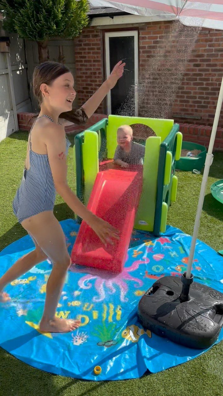 Children playing with a plastic slide and splash pad in a sunny backyard