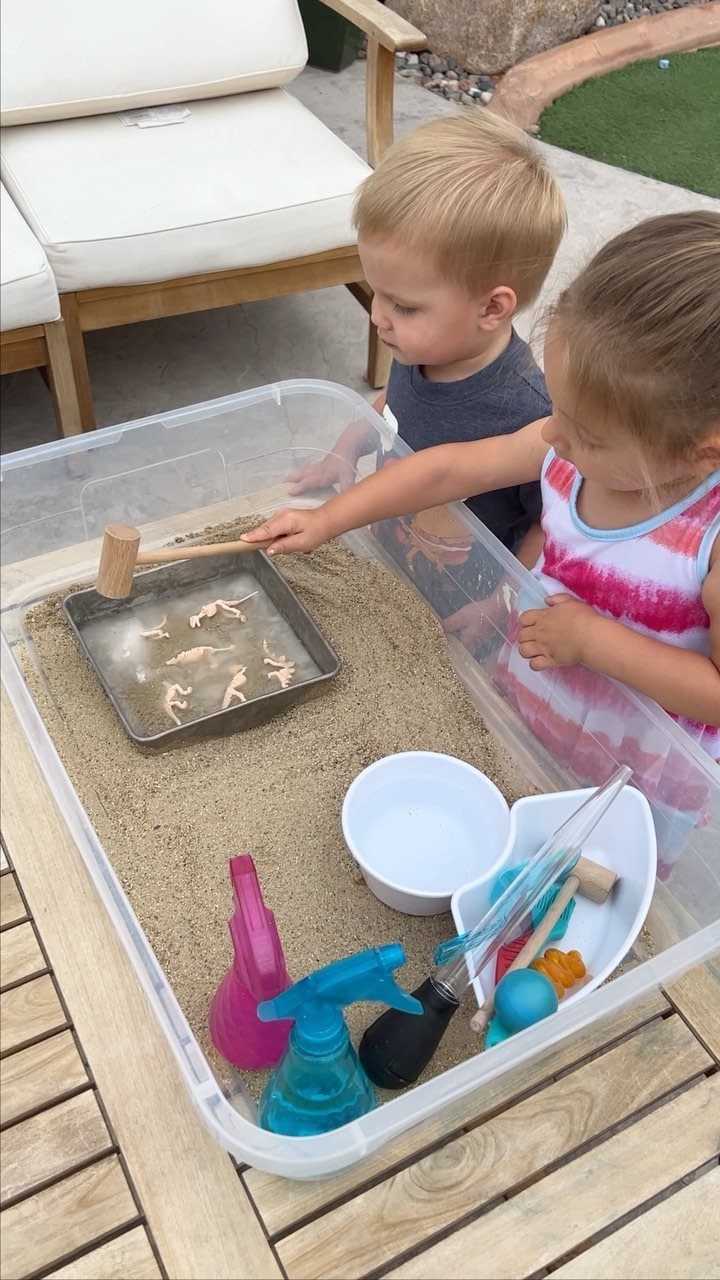 Two children using a wooden hammer to dig dinosaurs out of ice blocks.