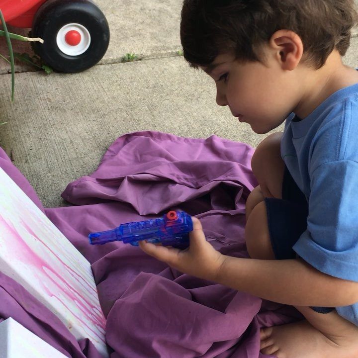 Young boy using a blue water gun to paint on a canvas outdoors