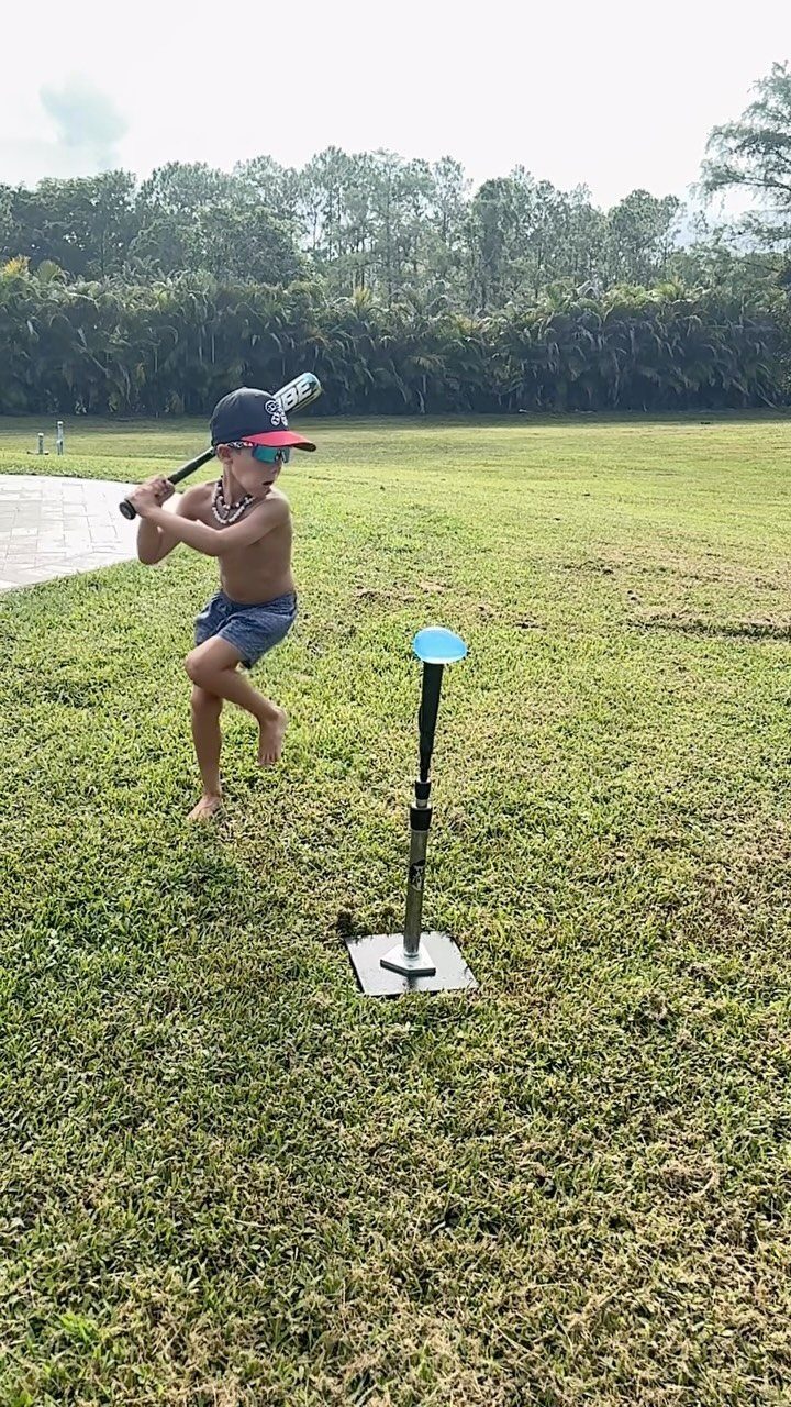 Boy swinging a baseball bat at a water balloon on a tee outdoors
