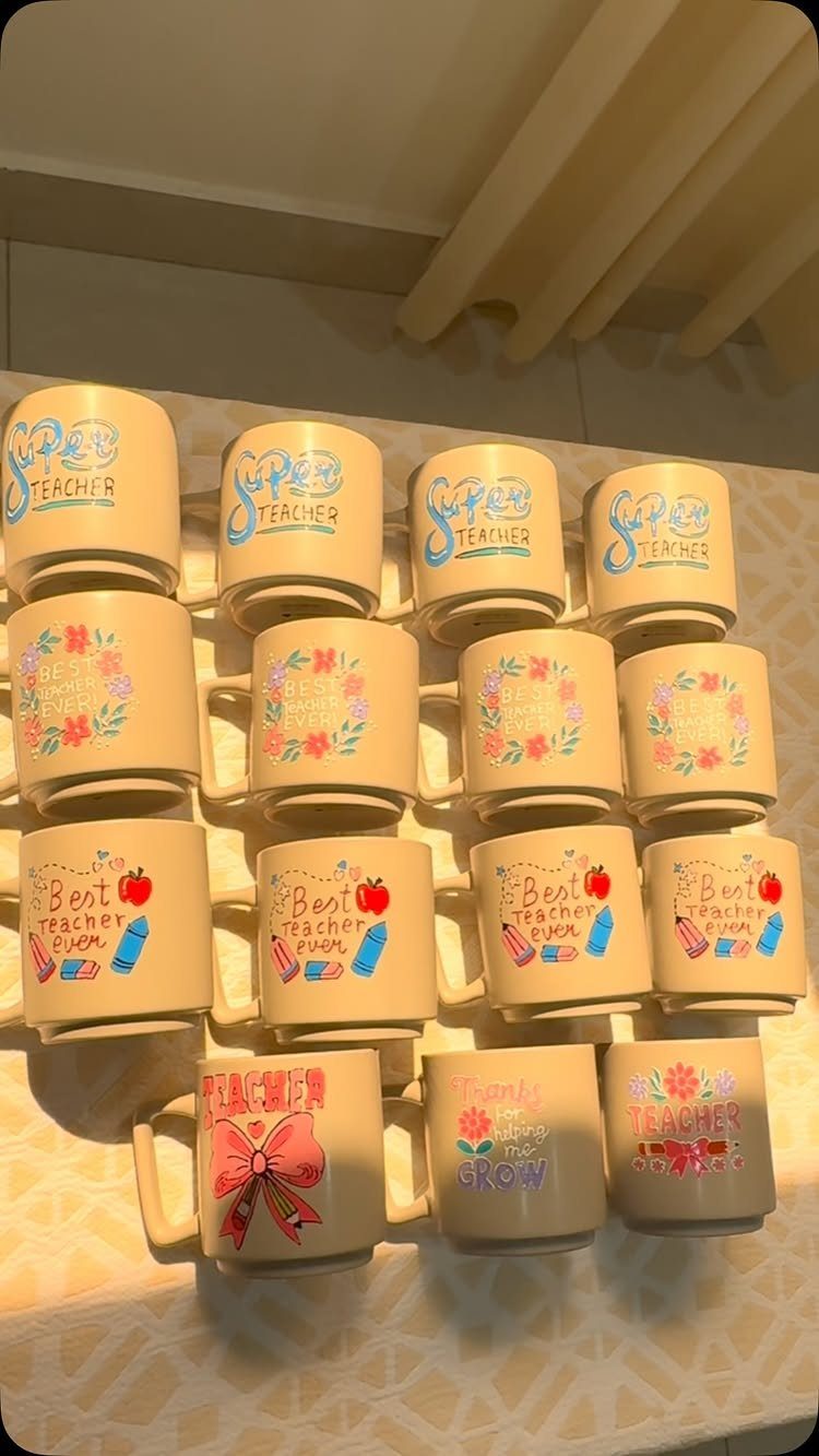 Beige coffee mugs with colorful teacher-themed prints arranged in rows on a table.