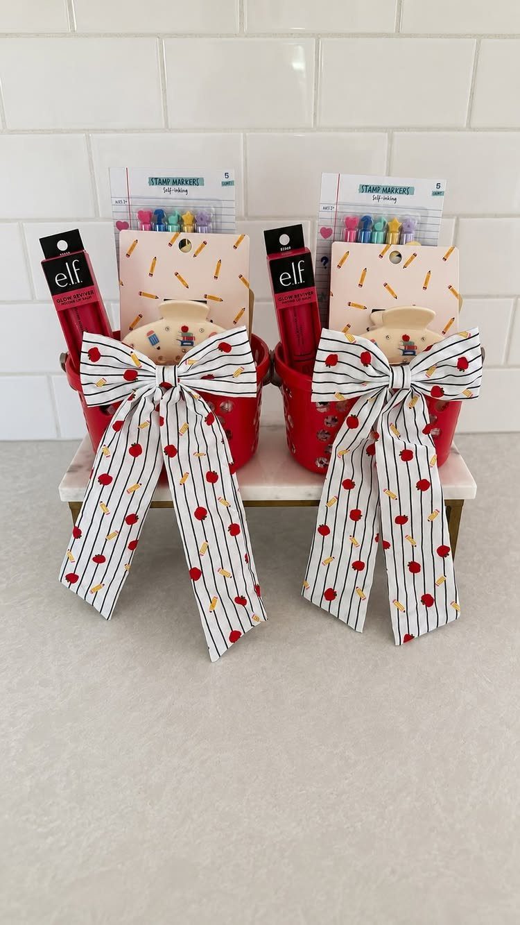 Two red gift buckets for teachers with apple-patterned ribbons and classroom supplies.