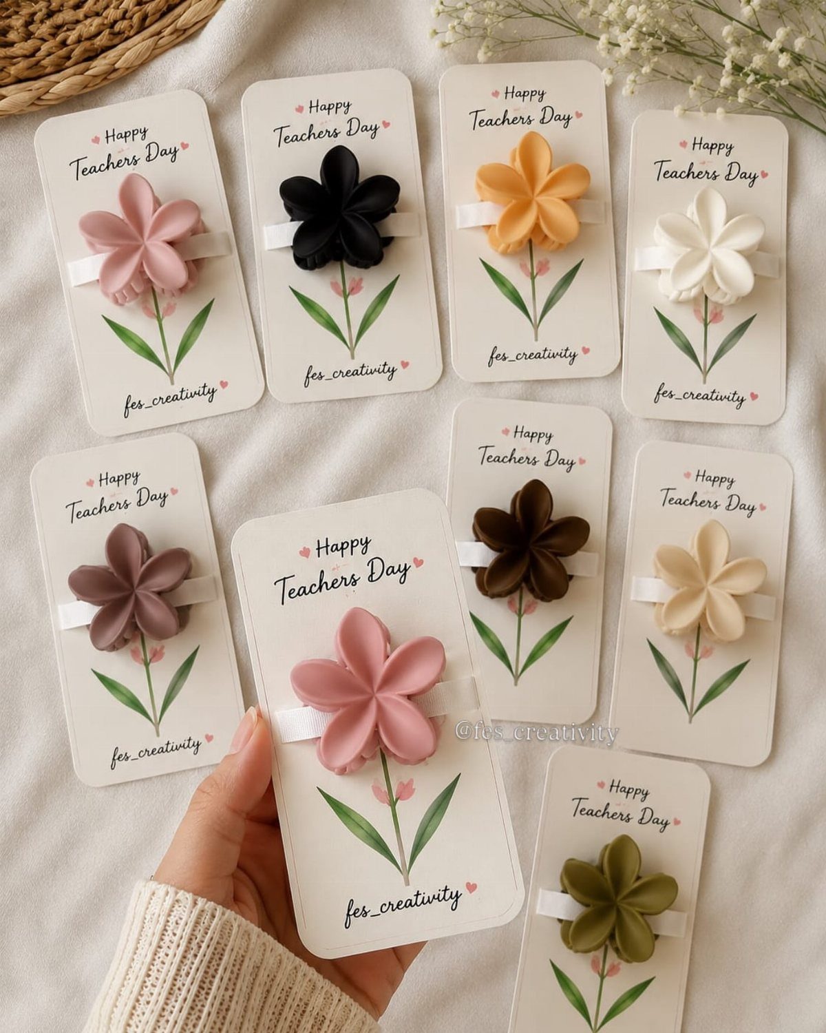 Flower-shaped accessories on Happy Teachers Day cards held by a hand on white fabric