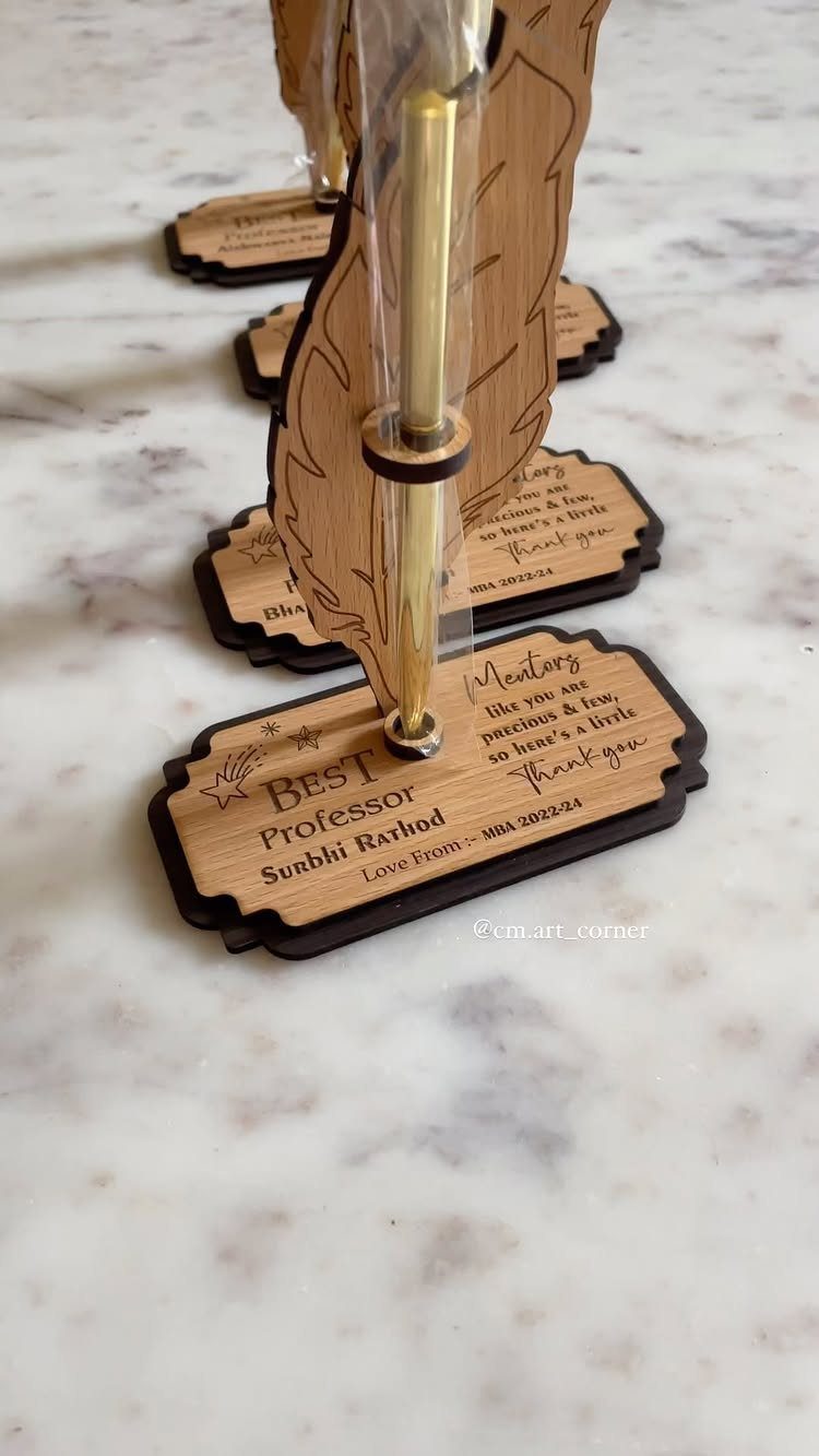 Wooden feather-shaped pen holders with engraved messages on a white marble surface