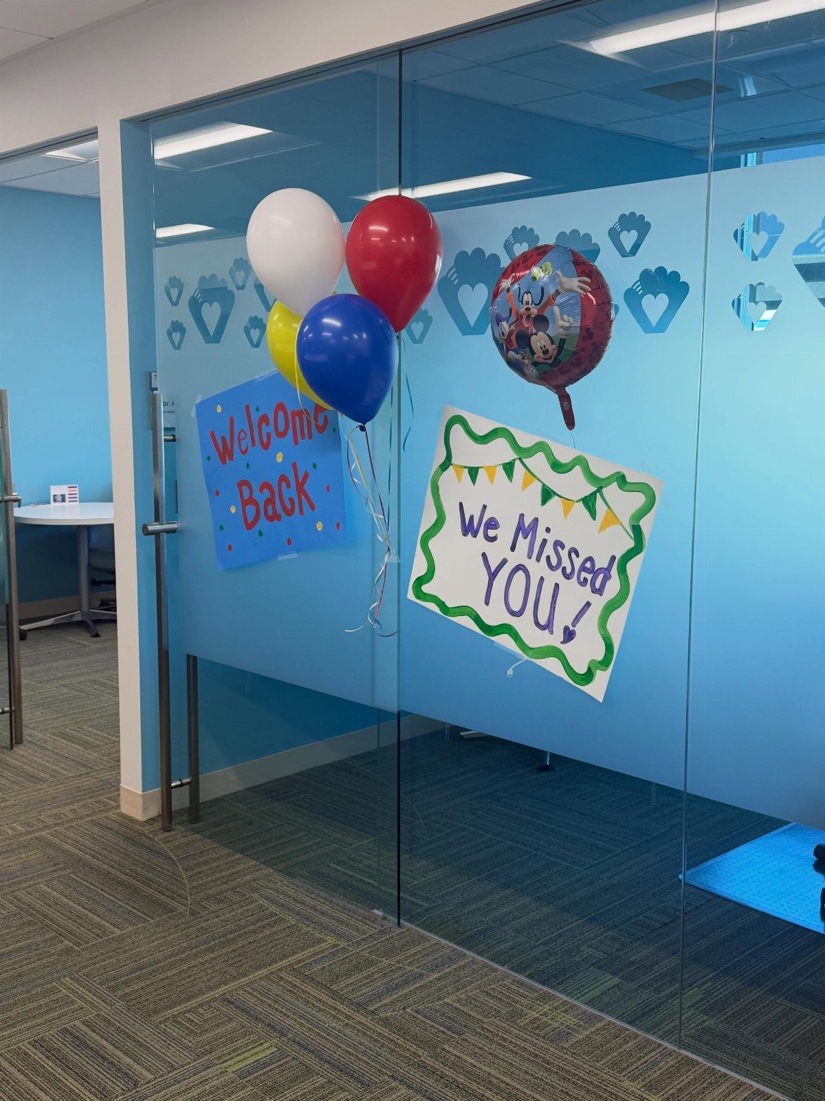 Balloons and welcome back signs attached to a blue glass office wall.