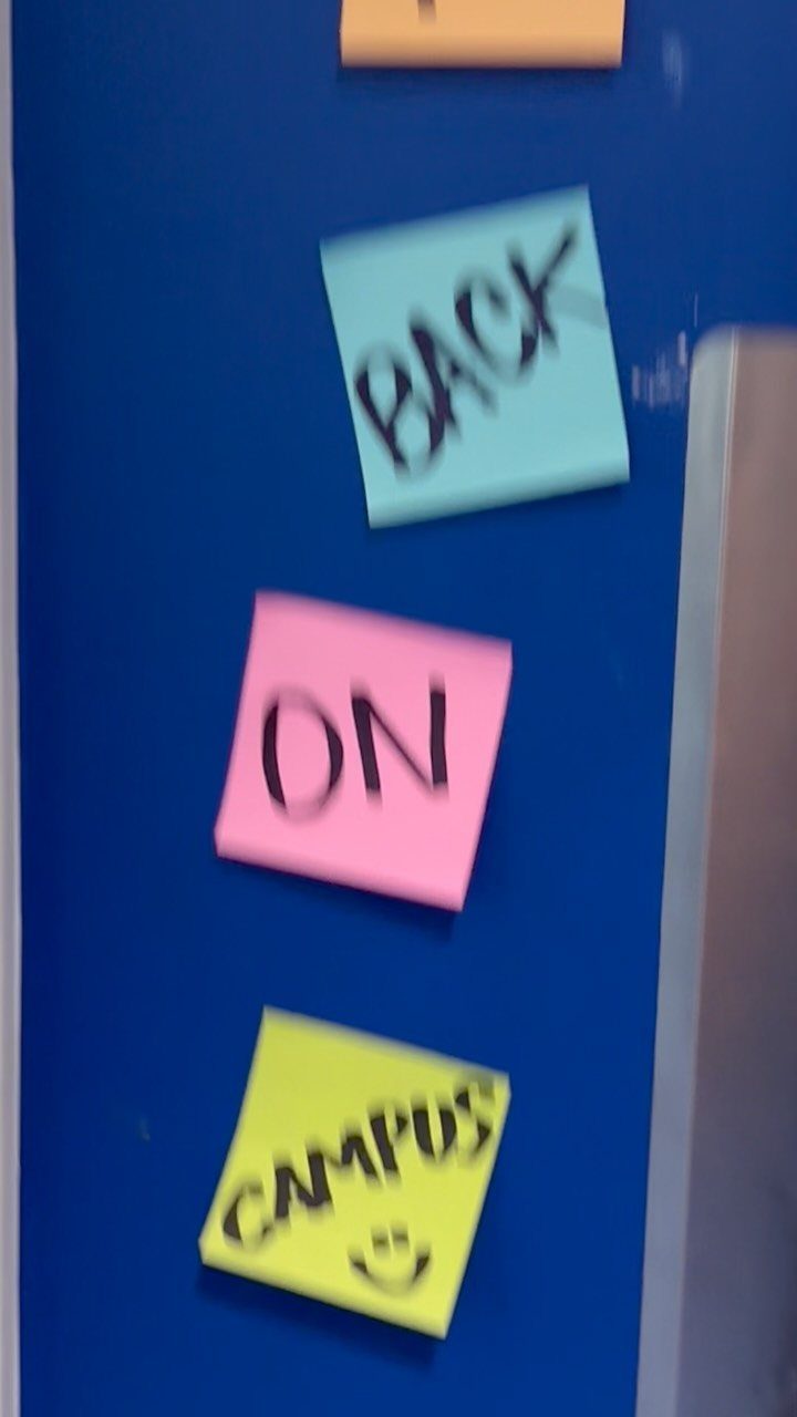Three colorful sticky notes on a blue wall saying BACK ON CAMPUS with smiley