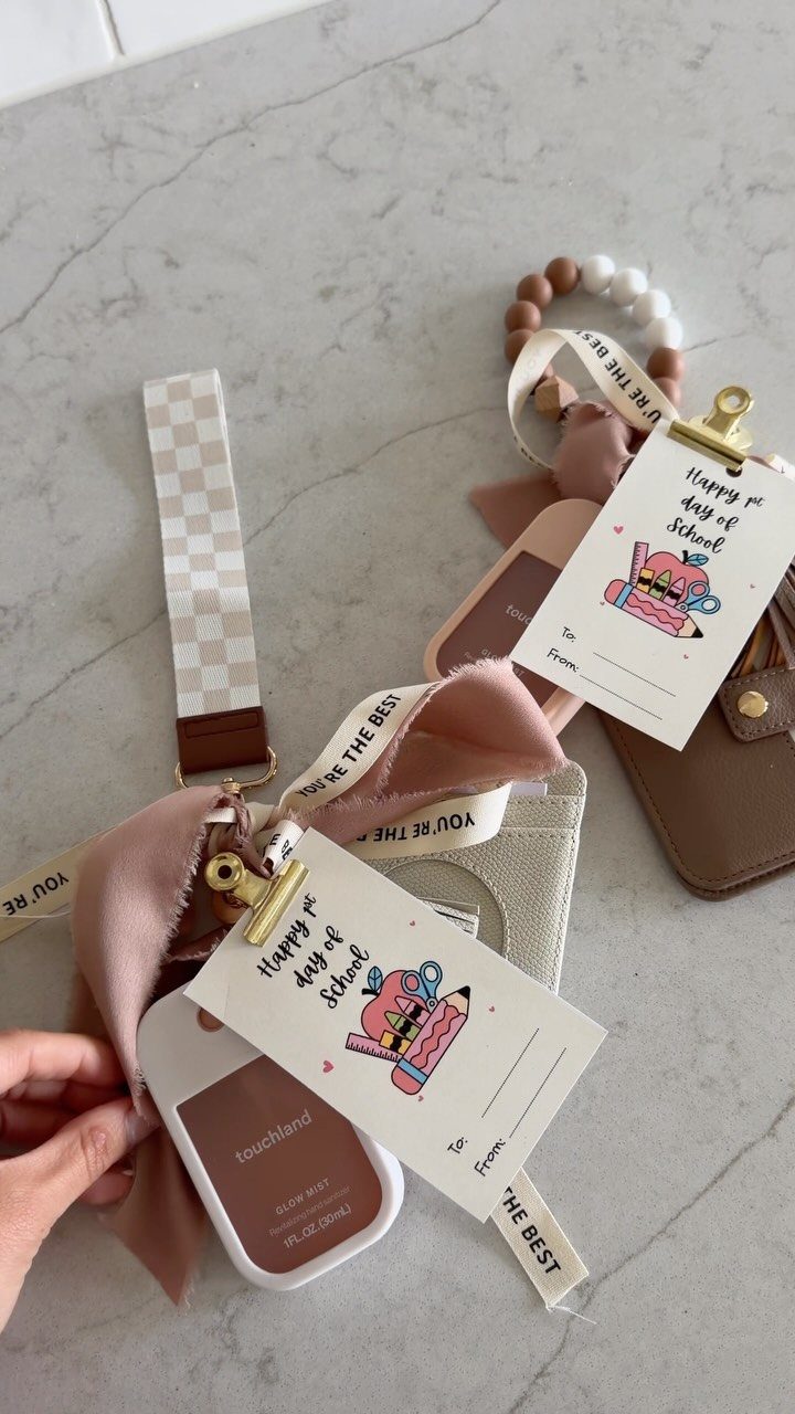 Hand sanitizer bottles with pink ribbons and school-themed gift tags on marble surface